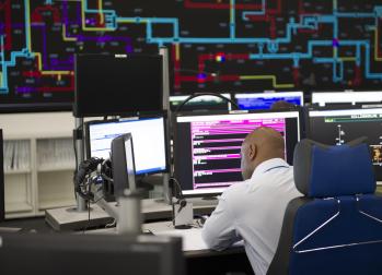 National Grid representative sitting in front of multiple computer monitors with a larger screen in the background displaying a pipe network