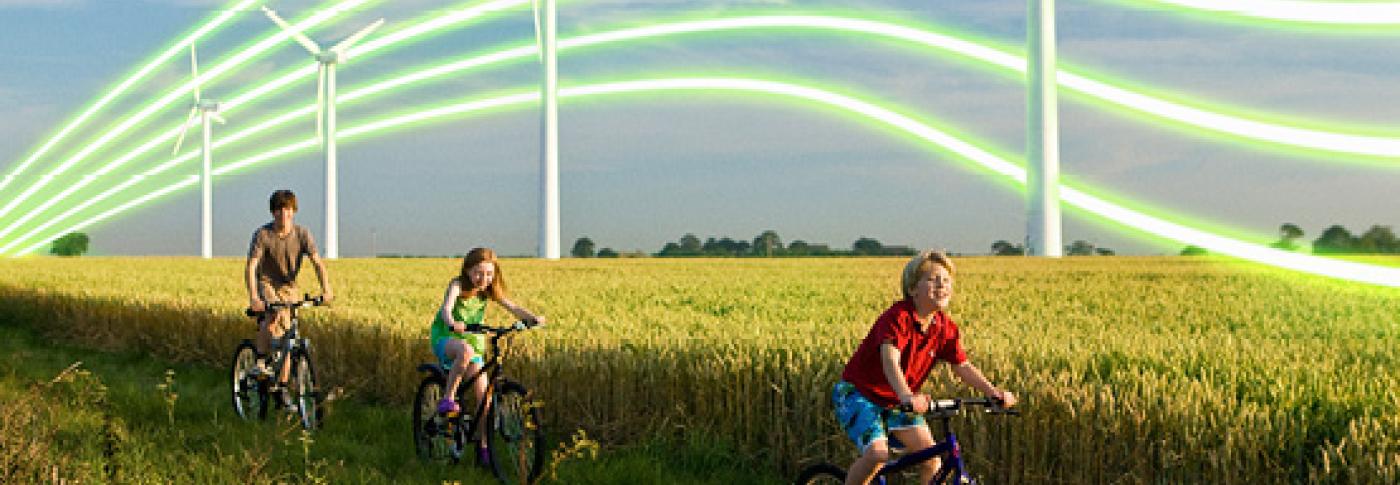 Family riding through field on bikes with wind turbines in distance SP