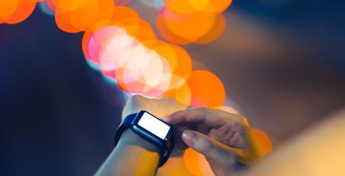 A partial view of an arm with a smart watch around the wrist and out of focus lighting in the background 