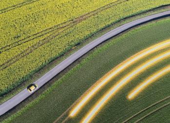 Aerial view of car driving on country road between fields